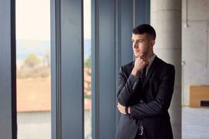 The confident businessman in a sleek suit strikes a pose, exuding charisma and professionalism, amidst the modern ambiance of the office. photo