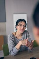 en un moderno oficina, un joven sonrisa mujer de negocios con lentes con confianza explica y regalos varios negocio ideas a su colegas, exhibiendo su profesionalismo y pericia. foto