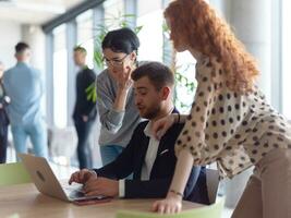 A businessman engaging in a discussion about sales statistics with his two female colleagues while they examine the data on a laptop in a modern office setting photo