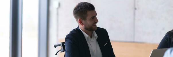 Wide crop photo of wheelchair bound businessman confidently leads a business meeting in a large, modern office, exemplifying inclusive leadership, effective communication, and the power of diversity in driving success and achieving impactful results.