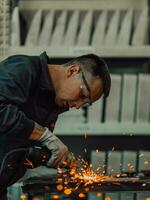 Heavy Industry Engineering Factory Interior with Industrial Worker Using Angle Grinder and Cutting a Metal Tube. Contractor in Safety Uniform and Hard Hat Manufacturing Metal Structures. photo