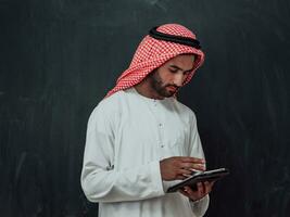 Young arabian muslim businessman using tablet computer wearing hijab clothes in front of black chalkboard photo