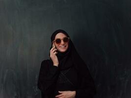 Young modern muslim business woman using smartphone wearing hijab clothes in front of black chalkboard photo