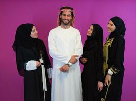 Group portrait of young muslim people arabian man with three muslim women in fashionable dress with hijab isolated on pink background representing modern islam fashion and ramadan kareem concept photo