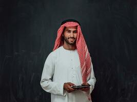 Young arabian muslim businessman using tablet computer wearing hijab clothes in front of black chalkboard photo