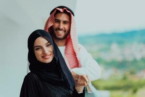 Portrait of young arabian muslim couple in traditional clothes standing on balcony representing modern islam fashion and ramadan kareem concept photo