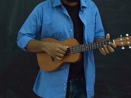 Indian young man in a blue shirt and glasses playing the guitar in front of the school blackboard photo