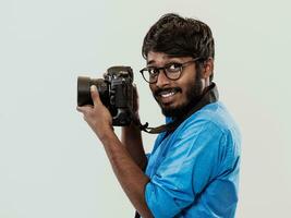 profesional fotógrafo teniendo dslr cámara tomando imagen.indio hombre fotografía entusiasta tomando foto mientras en pie en azul antecedentes. estudio Disparo