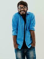 Indian smiling young man with blue shirt and glasses posing on gray background photo