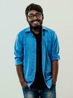 Indian smiling young man with blue shirt and glasses posing on gray background photo