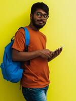 indio estudiante con azul mochila, lentes y cuaderno posando en gris y verde antecedentes. el concepto de educación y enseñanza. hora a Vamos espalda a colegio foto