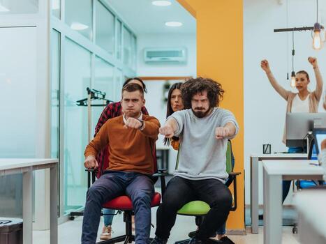 Team building and office fun. Young cheerful businesspeople in smart casual wear having fun while racing on office chairs and smiling. photo