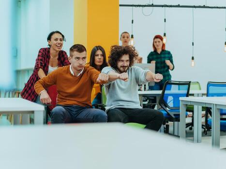 Team building and office fun. Young cheerful businesspeople in smart casual wear having fun while racing on office chairs and smiling. photo