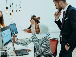 grupo de multiétnico colegas trabajando en escritorio ordenadores, ordenador portátil y compartiendo su ideas en un moderno oficina espacio.joven influencers trabajo en en línea márketing proyectos foto