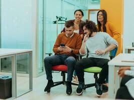 Team building and office fun. Young cheerful businesspeople in smart casual wear having fun while racing on office chairs and smiling. photo