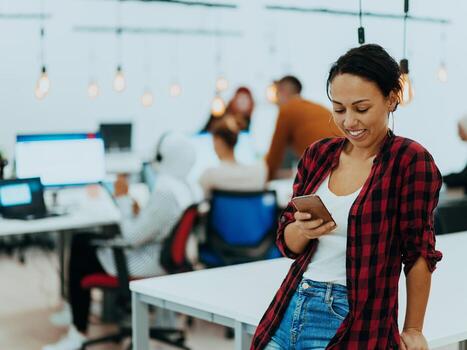 Woman sitting at workplace desk holds smartphone staring at laptop, synchronize data between computer and gadget in office, using corporate devices and business application, plan work, using organizer photo