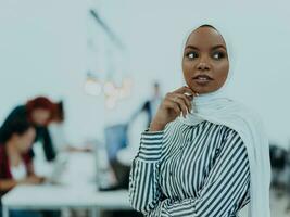 Portrait of a black african-american female muslim standing in a modern business office while wearing a hijab. photo