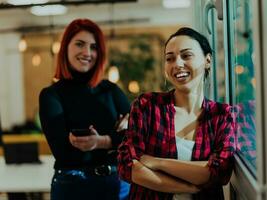 retrato de dos moderno joven mujer por el ventana en el noche oficina foto