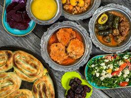 Eid Mubarak Traditional Ramadan Iftar dinner. Assorted tasty food in authentic rustic dishes on wooden blue background. Turkish Bosnian food meat kebab, pita, Sarma, klepe, sogan dolma. photo