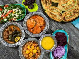 Eid Mubarak Traditional Ramadan Iftar dinner. Assorted tasty food in authentic rustic dishes on wooden blue background. Turkish Bosnian food meat kebab, pita, Sarma, klepe, sogan dolma. photo