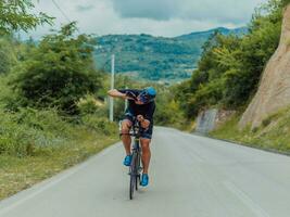 lleno longitud retrato de un activo triatleta en ropa de deporte y con un protector casco montando un bicicleta. selectivo atención foto