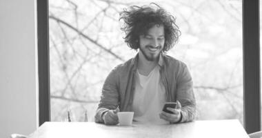 joven bebiendo café y usando un teléfono móvil en casa foto