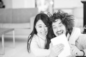 multiethnic couple using tablet computer in front of fireplace photo