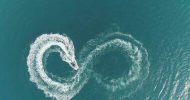 aéreo parte superior ver de un blanco Placer barco en un verano día. lancha fuera borda giro lazo ocho en el mar haciendo metaverso infinito futuro concepto. foto