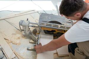 Man cutting laminate floor plank with electrical circular saw photo