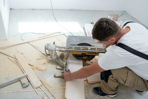 Man cutting laminate floor plank with electrical circular saw photo