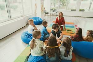 A happy female teacher sitting and playing hand games with a group of little schoolchildren photo