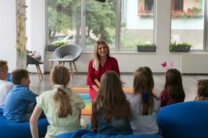 Reading time in an elementary school or kindergarten, a teacher reads a book to children in an elementary school or kindergarten. The concept of pre-school education. Selective focus photo