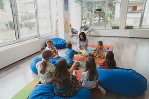 Reading time in an elementary school or kindergarten, a teacher reads a book to children in an elementary school or kindergarten. The concept of pre-school education. Selective focus photo