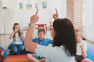 A happy female teacher sitting and playing hand games with a group of little schoolchildren photo