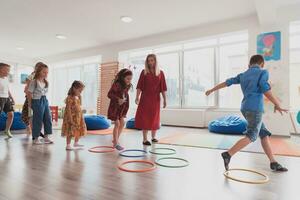 Small nursery school children with female teacher on floor indoors in classroom, doing exercise. Jumping over hula hoop circles track on the floor. photo