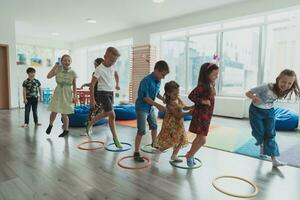 Small nursery school children with female teacher on floor indoors in classroom, doing exercise. Jumping over hula hoop circles track on the floor. photo