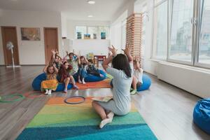 A happy female teacher sitting and playing hand games with a group of little schoolchildren photo