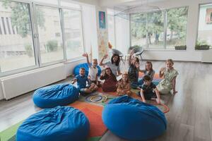 un contento hembra profesor sentado y jugando mano juegos con un grupo de pequeño Niños de escuela foto