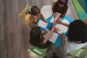 Creative kids during an art class in a daycare center or elementary school classroom drawing with female teacher. photo