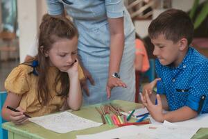 Creative kids during an art class in a daycare center or elementary school classroom drawing with female teacher. photo