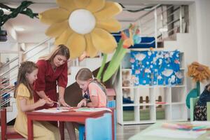 Creative kids during an art class in a daycare center or elementary school classroom drawing with female teacher. photo