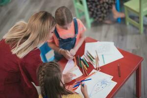 Creative kids during an art class in a daycare center or elementary school classroom drawing with female teacher. photo