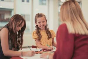 Creative kids during an art class in a daycare center or elementary school classroom drawing with female teacher. photo