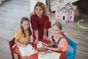 Creative kids during an art class in a daycare center or elementary school classroom drawing with female teacher. photo