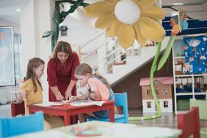 Creative kids during an art class in a daycare center or elementary school classroom drawing with female teacher. photo