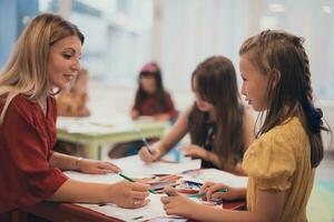 Creative kids during an art class in a daycare center or elementary school classroom drawing with female teacher. photo