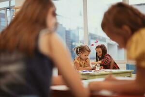 Creative kids during an art class in a daycare center or elementary school classroom drawing with female teacher. photo