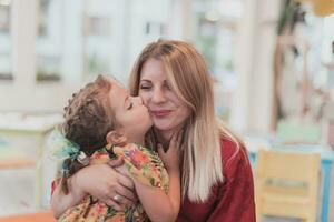 A cute little girl kisses and hugs her mother in preschool photo