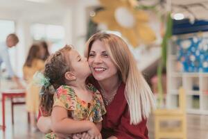 un linda pequeño niña Besos y abrazos su madre en preescolar foto