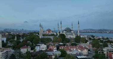 Establishing orbiting aerial drone shot of a Hagia Sophia Holy Grand Mosque with Bosphorus bridge and city skyline with a flag on the background in Fatih, Istanbul, Turkey at sunset. photo